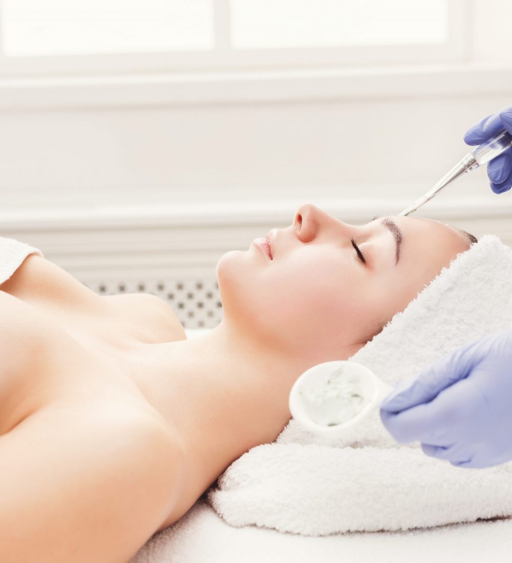 Face peeling mask, spa beauty treatment, skincare. Woman getting facial care by beautician at spa salon, side view, close-up